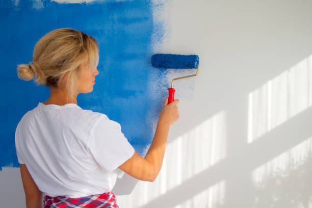 istock woman painting a wall with paint roller 1066487452