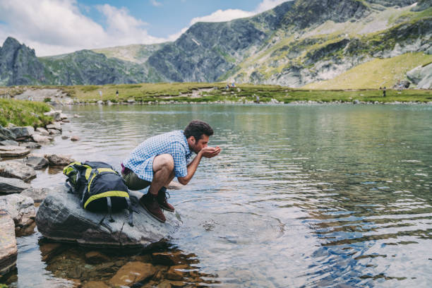 istock Tourist man drinking water from mountain lake 1066492380