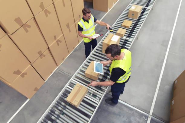 travailleur dans un entrepôt dans le secteur de la logistique traitement de paquets sur la ligne d’assemblage - transport et traitement des commandes dans le commerce - convoyeur photos et images de collection