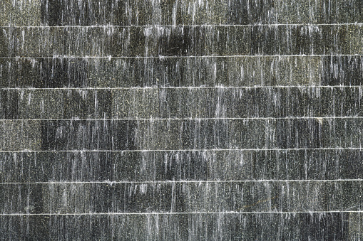 Surface picture of black stone with flowing water at  artificial waterfall.