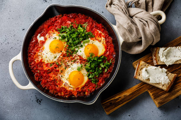 フライパンでトマトと shakshuka 揚げ卵を朝食し、柔らかい山羊チーズとパン - comfort food ストックフォトと画像