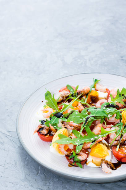 istock Appetizing salad of cherry tomatoes, eggs, boiled shrimps, arugula, sesame seeds and balsamic sauce in a plate 1066513938