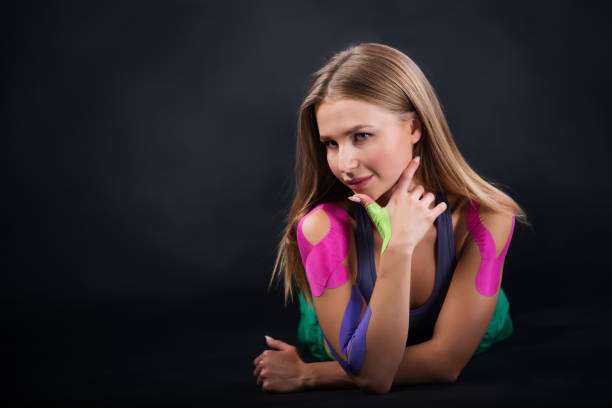 Beautiful sport girl posing on a gray background, kinesio tape