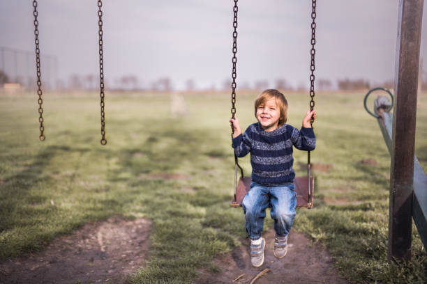 Cute smiling boy swinging in nature and looking at camera.