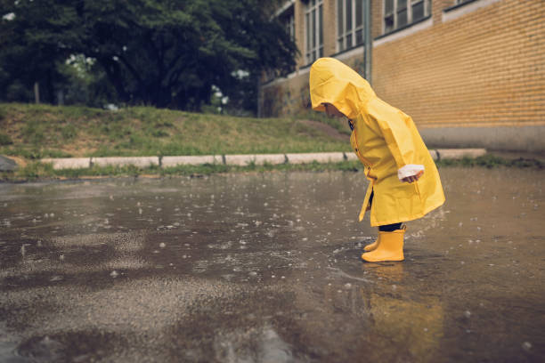 Adorable little boy playing at rainy day Little boy walking outdoors at rainy autumn day raincoat photos stock pictures, royalty-free photos & images