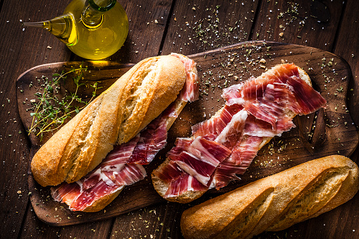 Typical spanish food concepts: High angle view of a rustic wooden table with two delicious Iberico ham sandwich also called in Spain as Bocadillo de Jamón Iberico. Predominant color is brown. Low key DSRL studio photo taken with Canon EOS 5D Mk II and Canon EF 100mm f/2.8L Macro IS USM.