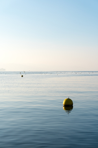 vertical minimalist view of blue lake with blue sky and yellow floating buoy and distance marker on Lake Zurich near Rapperswil