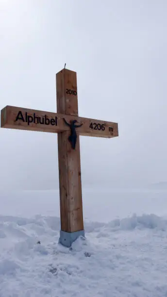 wooden summit cross on the Alphubel mountain peak between Saas Fee and Zermatt covered in deep snow in winter