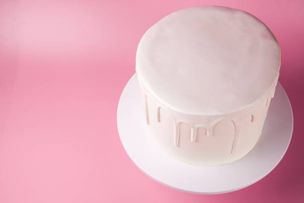 Simple white cake with white glaze on a pink background.