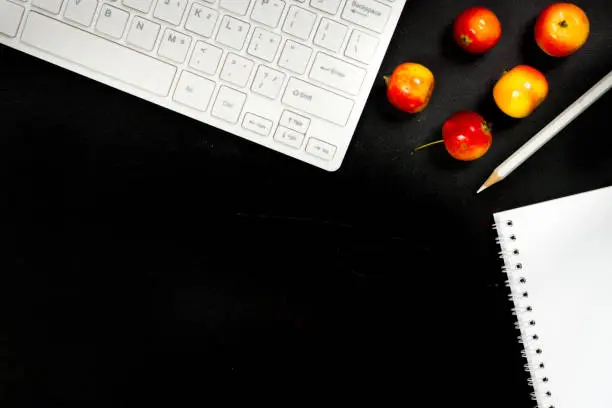 black table with white office equipment and red small apples