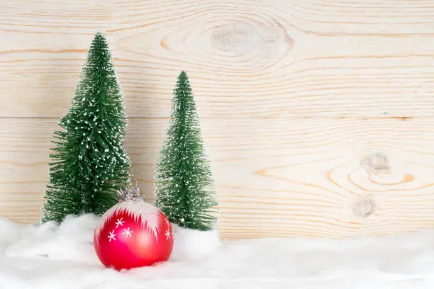two evergreen fir trees and red ball, snowy christmas composition, wooden background, copy space