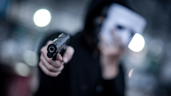 Mystery hoodie man in white mask pointing gun. Crime and violence concepts. Focus on gun