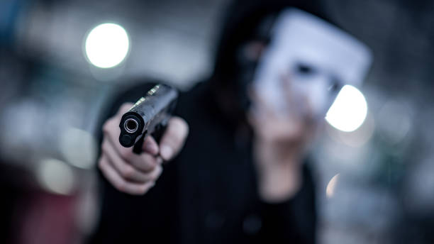 Mystery hoodie man in white mask pointing gun. Crime and violence concepts. Focus on gun Mystery hoodie man in white mask pointing gun. Crime and violence concepts. Focus on gun gun control photos stock pictures, royalty-free photos & images