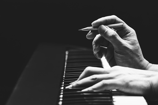 male songwriter hands composing a song on piano, black and white. song writing concept