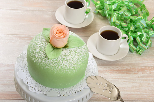 Traditional Swedish princess cake or prinsesstårta made with vanilla sponge cake, creme, raspberry jam and covered with green marzipan, served with coffee.