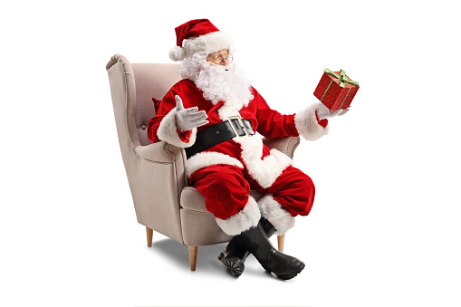 Santa Claus sitting in an armchair and holding a present isolated on white background