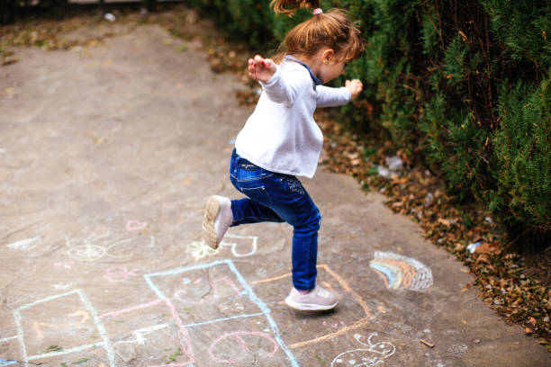 активная маленькая девочка, наслаждающаяся игрой в хопскотч - hopscotch стоковые фото и изображения