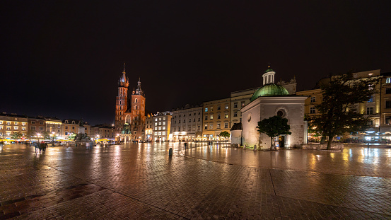 Krakow, Poland - October 21, 2018: Krakow  view showing Old town square, Main market square, St. Mary's Church, buildings, restaurants, trees and people walking on the street can be seen on the background at night