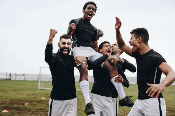 soccer players celebrating success by lifting a teammate on shoulders - equipa desportiva imagens e fotografias de stock