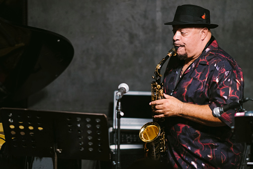 An African American senior man is playing the saxophone at stage during a jazz music concert.