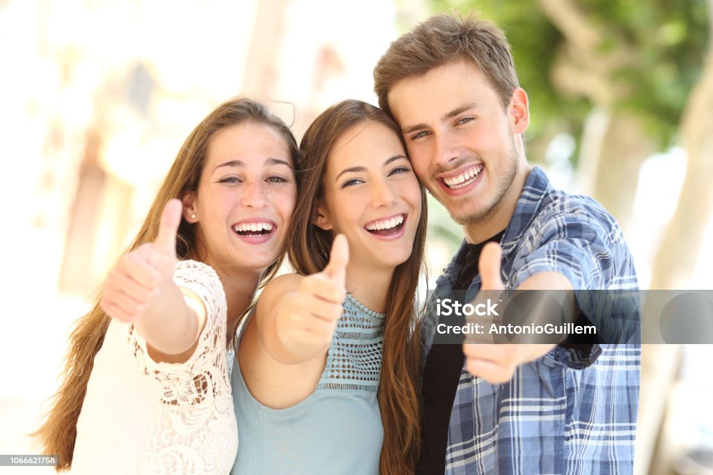 Three happy friends smiling with thumbs up in the street Front view portrait of three happy friends smiling with thumbs up in the street Teenager Stock Photo