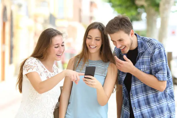 Three happy friends watching smartphone content in the street