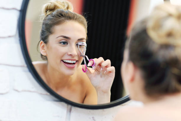 Young woman using eyelash curler in bathroom