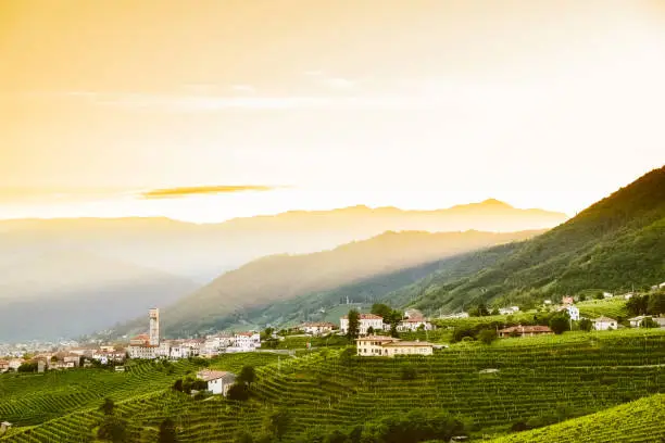 small italian town of valdobbiadene in veneto region on green hills at sunset with prosecco vineyards
