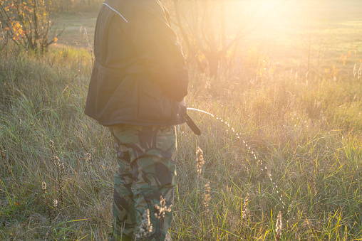 A man in camouflage pants pees on the nature in the grass