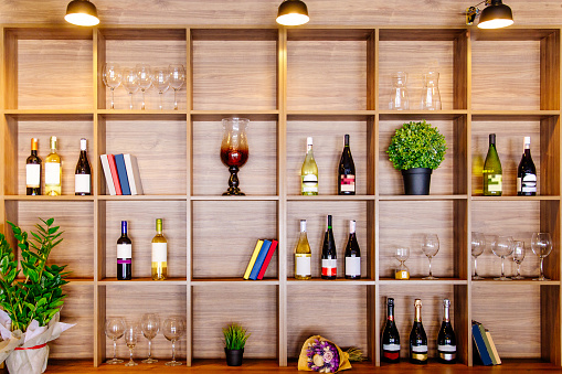 Bottles of white and red wine on a wooden shelf with books in private winery cabinet room interior.