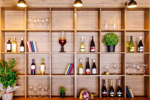 Photo of Bottles of white and red wine on a wooden shelf with books in private winery cabinet room interior