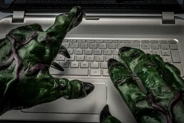 Cyber bullying, online fraud, computer virus or internet trolls concept with the hands of a troll typing on the keyboard of a laptop computer