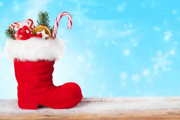 Santa boots with sweets and gifts on a blue background with falling snowflakes