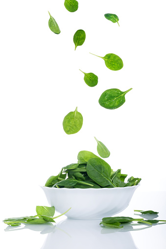 Green spinach leaves flying on white, fresh salad in motion, vegetables levitation concept