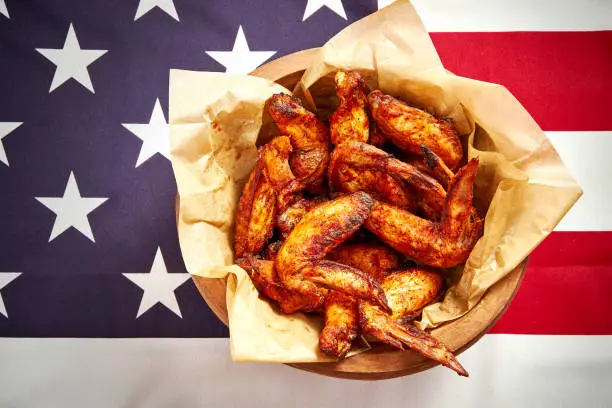 top view of delicious fried chicken wings in a bowl with sauces on the background of the USA flag