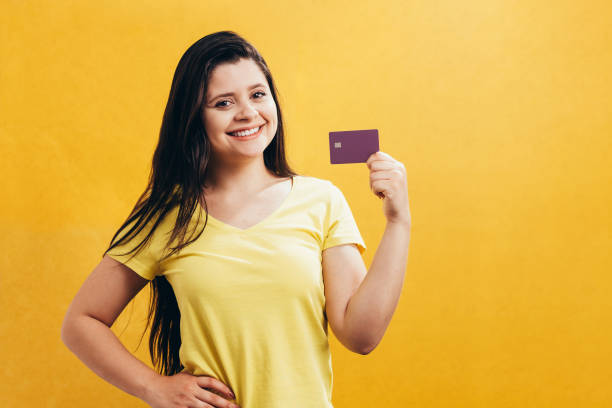 ritratto di una ragazza felice che mostra carta di credito di plastica isolata su sfondo giallo - showing buying paying clipping path foto e immagini stock