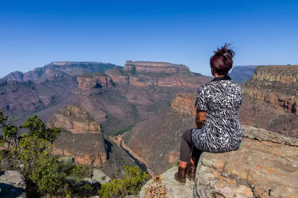 View of Three Rondavels in Blyde River Canyon, South Africa. Woman poses near cliff edge and looks at view.