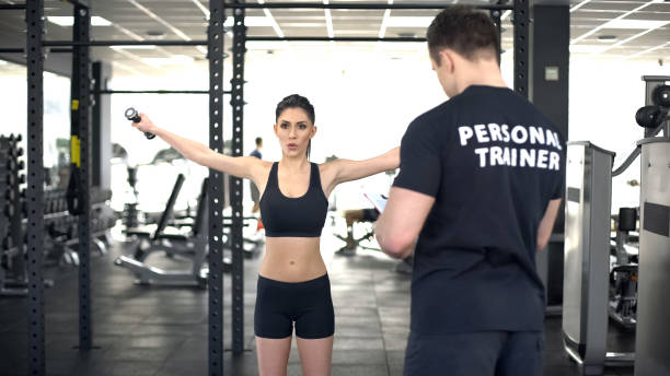 istock Active woman doing exercise with dumbbells during workout with personal trainer 1066730050