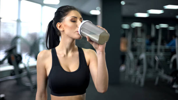 sporty woman drinking protein shake after workout, muscle gain nutrition, health - nutritional supplement fotos imagens e fotografias de stock