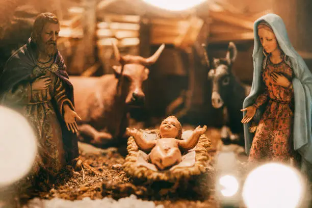 An old Christmas nativity set, with Joseph, Mary, and the baby Christ child in a manger.  Animals and visitors also visible in the classic scene.  A warm holiday background.