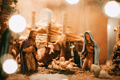 An old Christmas nativity set, with Joseph, Mary, and the baby Christ child in a manger.  Animals and visitors also visible in the classic scene.  A warm holiday background.