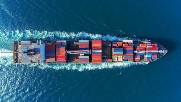 Photo of Aerial view Top speed with beautiful wave of container ship full load container with crane loading container for logistics import  export or transportation concept background.