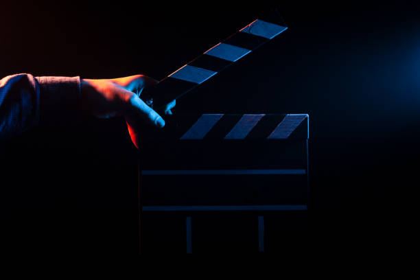 istock Opened clapperboard for cinema in hand, before filming on a black isolated background with red and blue backlighting 1066783908