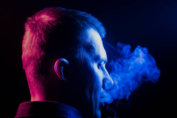 タバコを吸うことと吐くことのシャツを着た少年の首の後ろから見た黒い自身から右側に青の複数の色の煙が背景を分離しました。健康に害を与えます。 - smoke condensation fumes isolated ストックフォトと画像