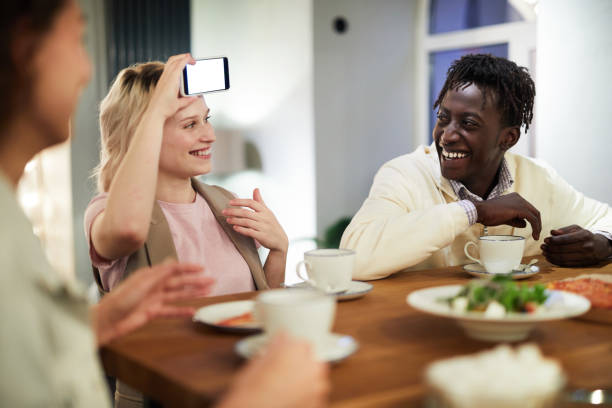 istock Joyful young multi-ethnic friends sitting at table with food and drinking tea while playing game in cafe: cheerful African guy with dreads laughing while girl guessing word on her forehead 1066794978