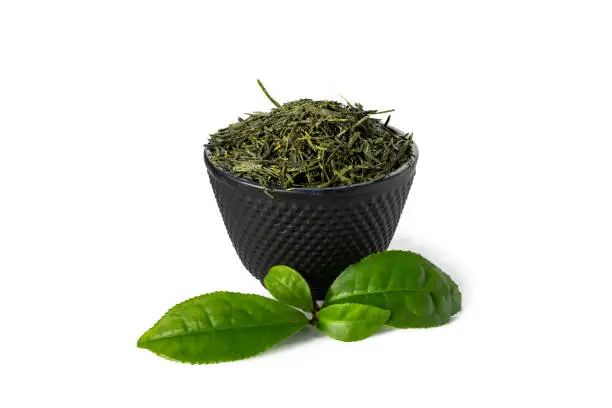 Green sencha tea in black cast iron cup with tealeaves in front isolated on white background.