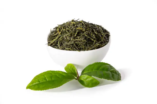 Green sencha tea in white cup with tealeaves in front isolated on white background.