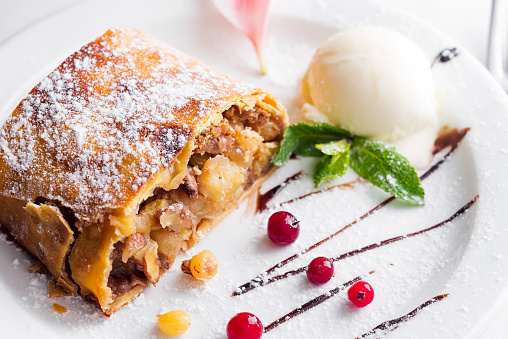Apple strudel with vanilla ice cream and mint and berries on white plate, close up