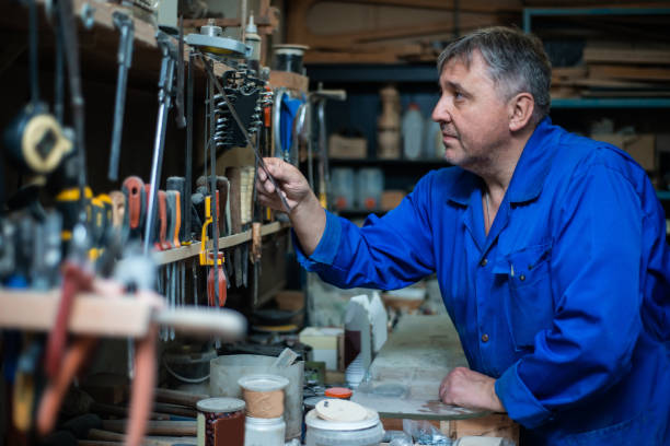 istock Mature man carpenter in overalls chooses tools in the workshop 1066868066