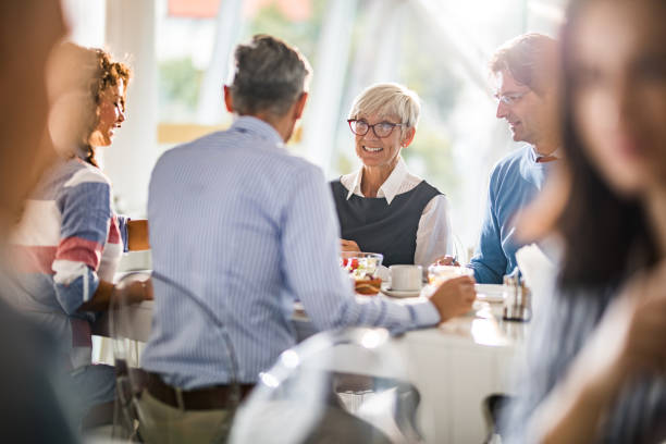 felice imprenditrice senior che parla con i suoi colleghi durante una pausa pranzo. - lunch foto e immagini stock